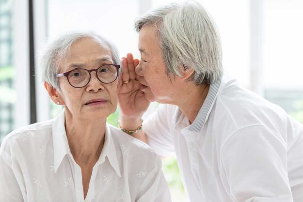 Asian senior woman holding hand near mouth telling funny,gossips Asian senior woman holding hand near mouth telling funny,gossips on ears to friend,speaking in elderly woman ear and near face