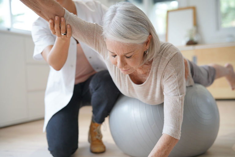 Senior woman exercising with her physiotherapist and swiss ball