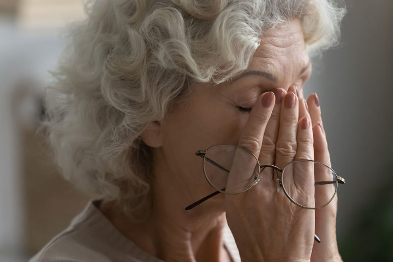 Close up of tired elderly woman rub massage eyes take off glasses suffering from headache or migraine