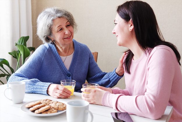 A daughter visits an elderly mother and they talk together at breakfast A daughter visits an elderly mother and they talk together at breakfast