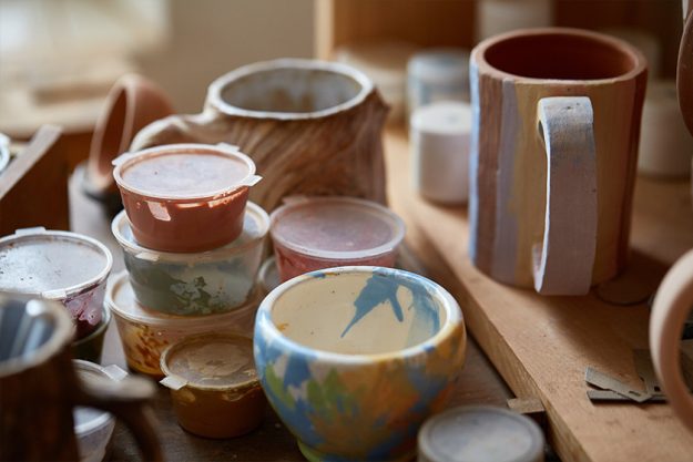various paint mugs and brushes in holder on worktop, selective focus