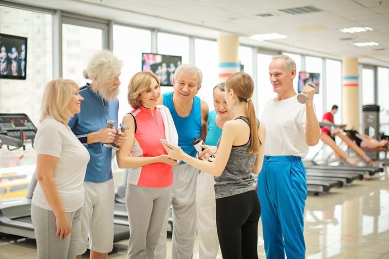 Group of elderly people and trainer with phone in gym
