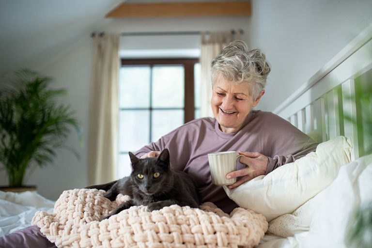 Happy senior woman with cat resting in bed at home