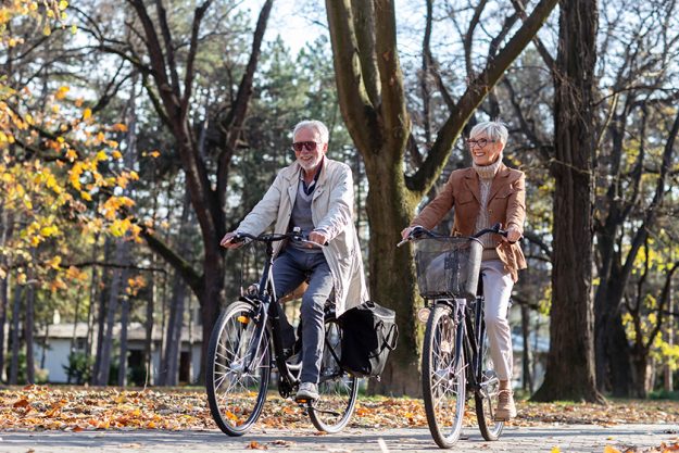 Mature fit couple ride in bicycles thru public park Mature fit couple ride in bicycles thru public park