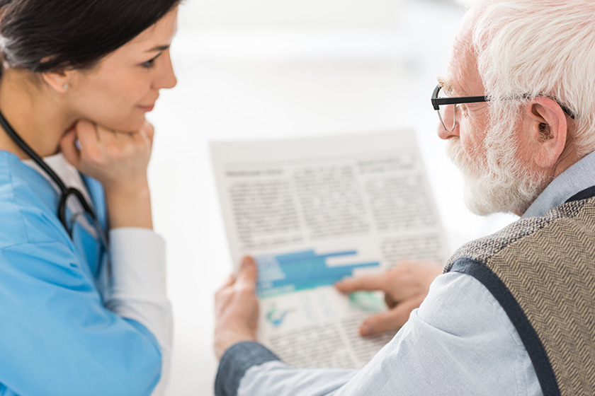 Selective focus of grey haired man talking with nurse, holding newspaper in hands Selective focus of grey haired man talking with nurse, holding newspaper in hands
