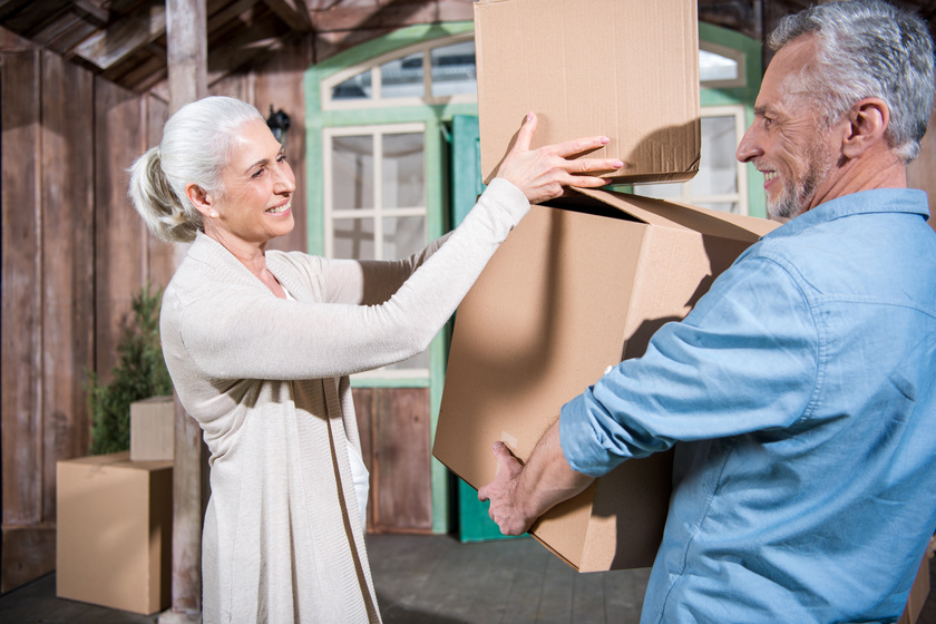 Smiling senior couple holding cardboard boxes while moving into Smiling senior couple holding cardboard boxes while moving into