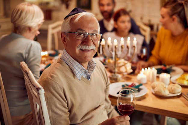 Happy Jewish senior man celebrates Hanukkah with his family at dining table. Happy Jewish senior man celebrates Hanukkah with his family at dining table.