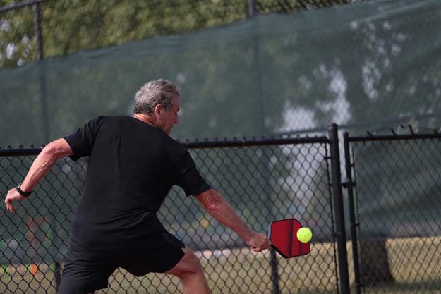 A senior athlete hits a shot, competing in singles, of a pickleball tournament