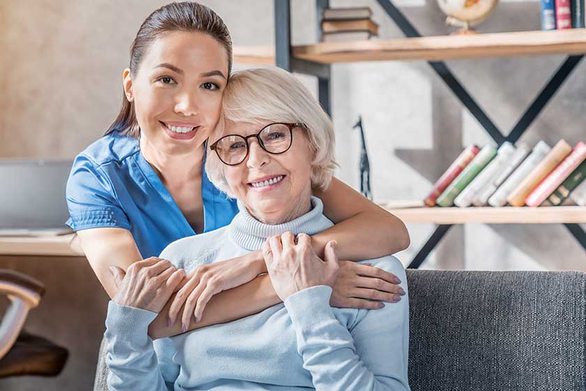 Portrait of female caretaker hugging happy elderly woman indoors