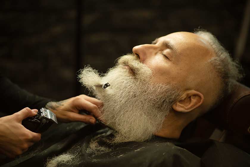 Handsome senior man getting styling and trimming of his beard in the barbershop.