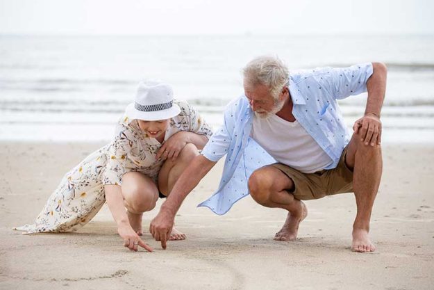 senior couple sitting on the beach drawing a heart in the sand together senior couple sitting on the beach drawing a heart in the sand together