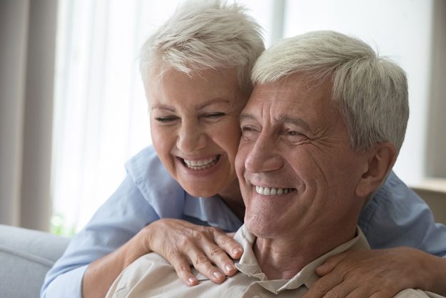 smiling middle aged wife embrace husband pensioner from behind massage shoulders smiling middle aged wife embrace husband pensioner from behind massage shoulders