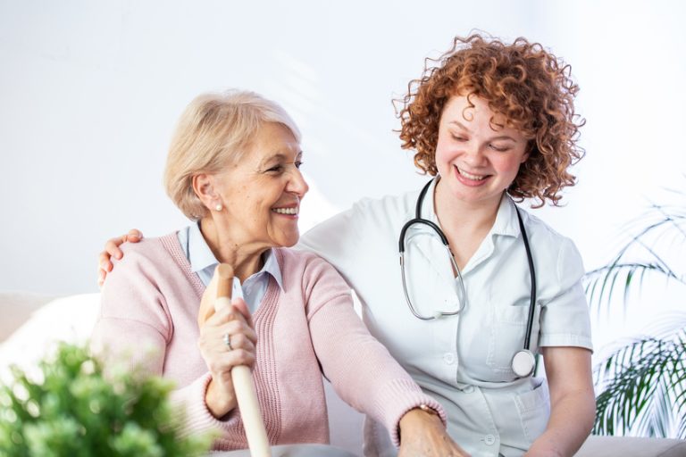 Young caregiver and senior woman laughing together while sitting on sofa. Senior woman and younger friend having fun together during meeting at home. What Makes An Effective Dementia Care? 3 Fundamentals