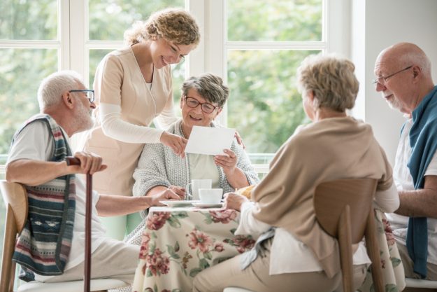 Group of seniors drinking tea together. Nurse is showing a photo Group of seniors drinking tea together. Nurse is showing a photo
