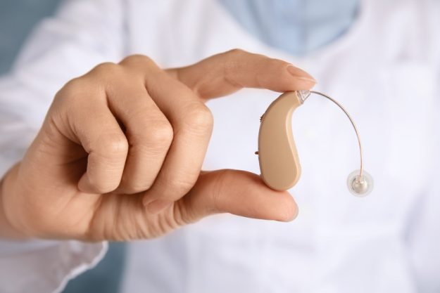 Doctor holding hearing aid, closeup. Medical device Doctor holding hearing aid, closeup. Medical device