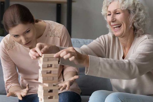 Excited mature woman with adult daughter playing funny stack and crash board game