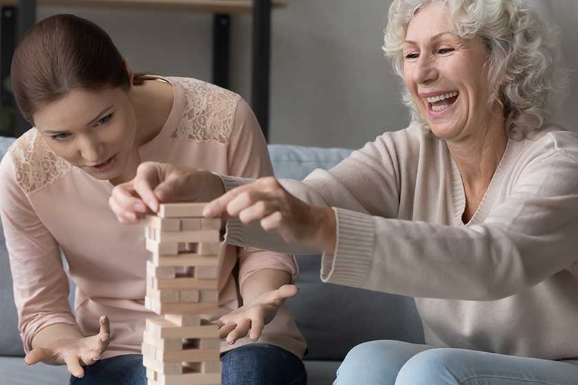 Excited mature woman with adult daughter playing funny stack and crash board game