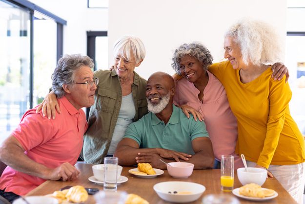 Multiracial senior friends with arms around enjoying by breakfast