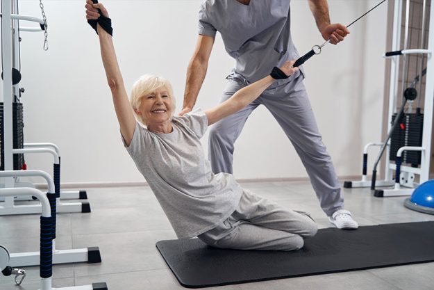 Aged woman leaning left while holding cable machine straps