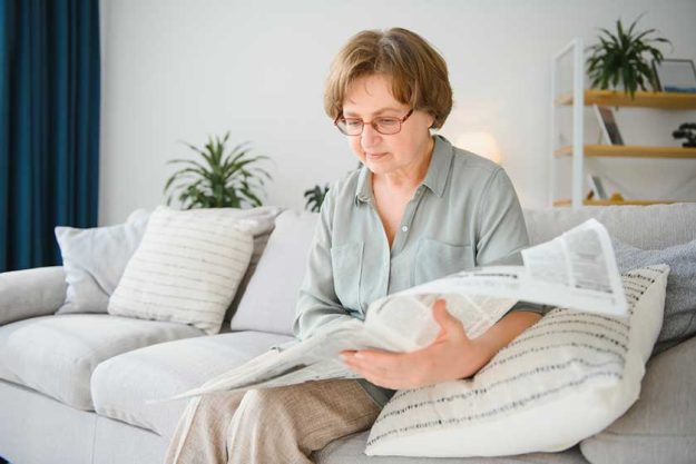 Senior lady reading her newspaper at home relaxing