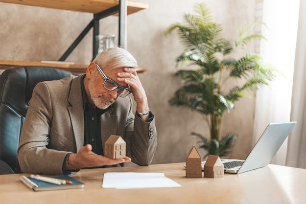 Senior man holding a model house in his hands in despair