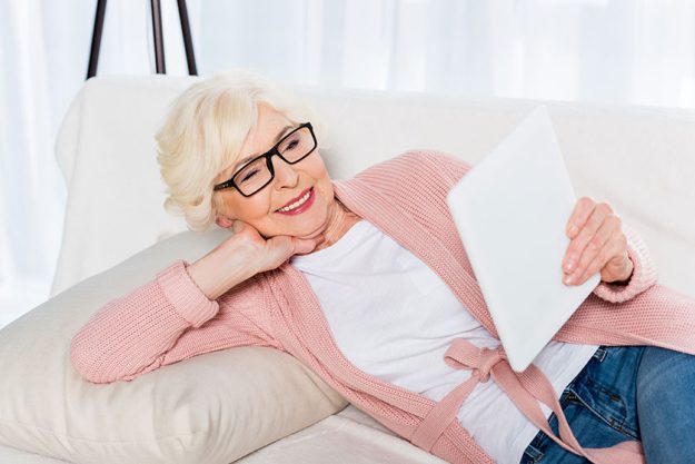 Smiling Senior Woman Eyeglasses Using Tablet While Resting Sofa