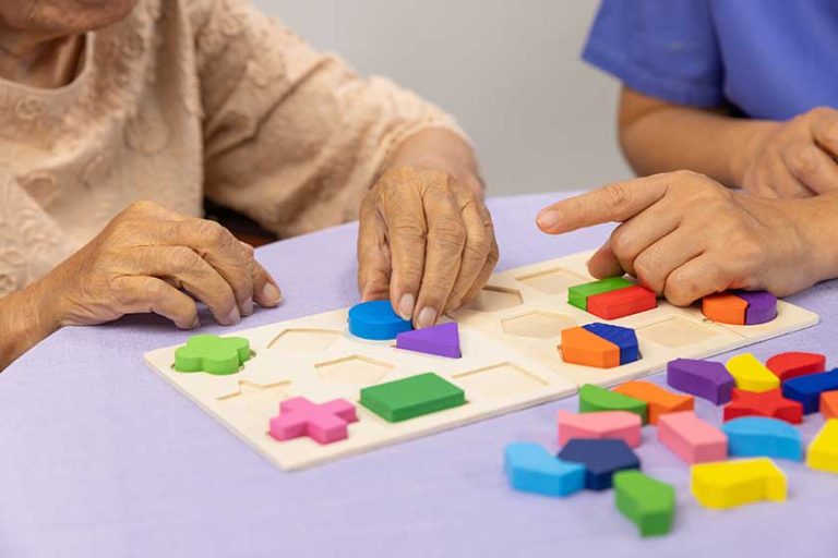 Caregiver and senior woman playing wooden shape puzzel Caregiver and senior woman playing wooden shape puzzel