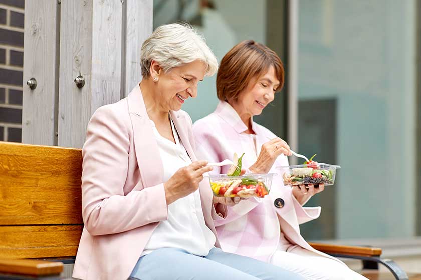 Senior women eating takeaway food on city street Senior women eating takeaway food on city street
