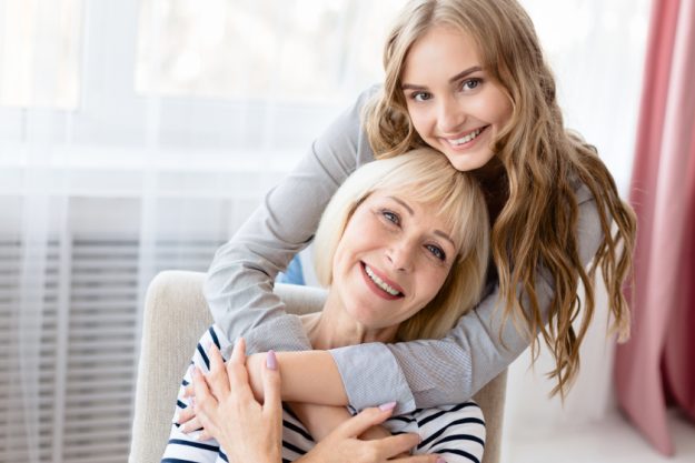 Daughter hugging senior mother and looking at camera
