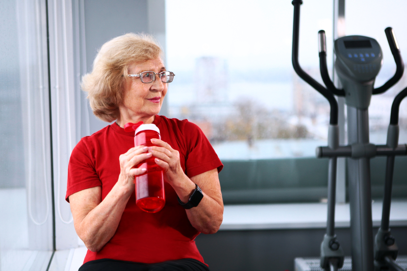 An elderly woman holds a water bottle in the gym. Active retirement lifestyle concept. Copy space.
