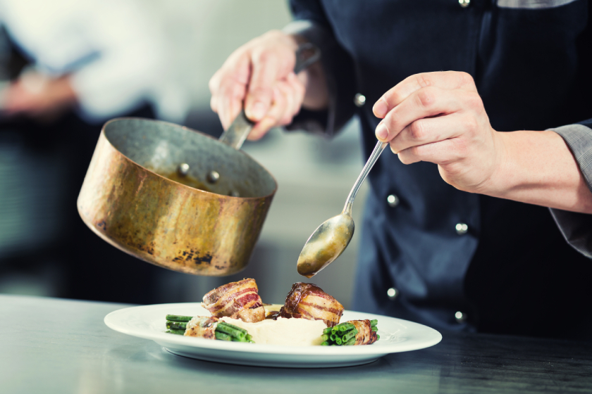Chef pouring sauce on dish in restaurant kitchen