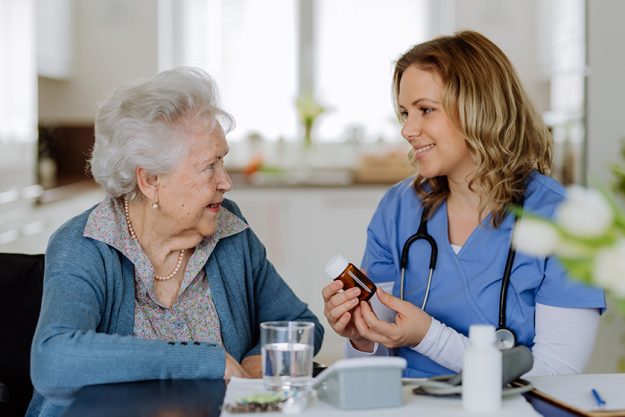 Nurse giving pills to senior woman in her home