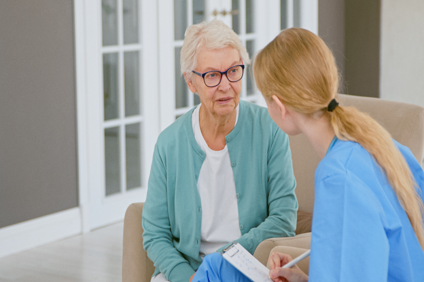 Young blonde doctor interviews short haired senior lady patient making notes in pad at appointment Young blonde doctor interviews short haired senior lady patient making notes in pad at appointment