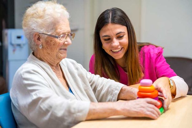Cute nurse helping woman play board skill game nursing home Cute nurse helping woman play board skill game nursing home
