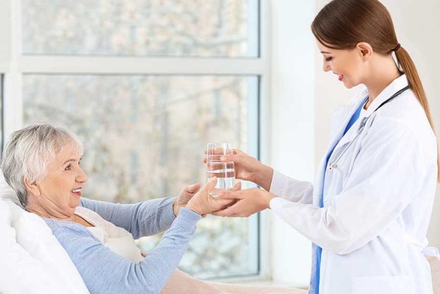 Female doctor giving senior woman suffering from Parkinson syndrome glass of water in clinic Female doctor giving senior woman suffering from Parkinson syndrome glass of water in clinic