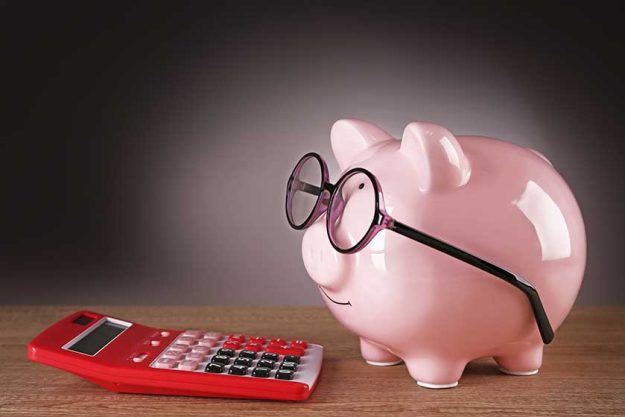Piggy bank in glasses with calculator on grey background Piggy bank in glasses with calculator on grey background