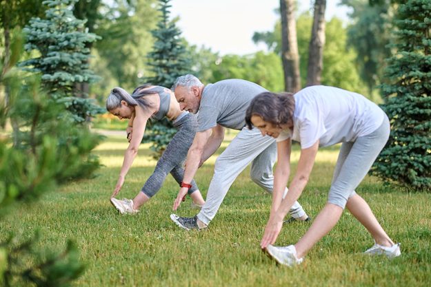 Sport in park. Mature group of people exercising outdoors, healthy lifestyle, stretching body before workout