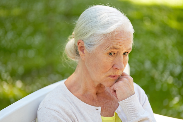 Sad senior woman sitting on bench at summer park