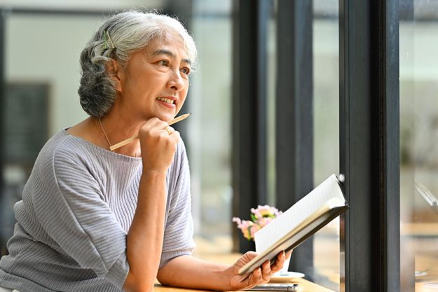 beautiful gray haired mature woman holding book looking away daydreaming