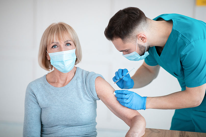 doctor in medical mask giving covid 19 vaccine shot to senior female patient during immunizatio