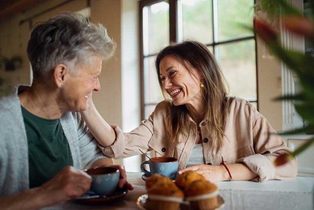 happy senior mother having tea with adult daughter indoors at home talking