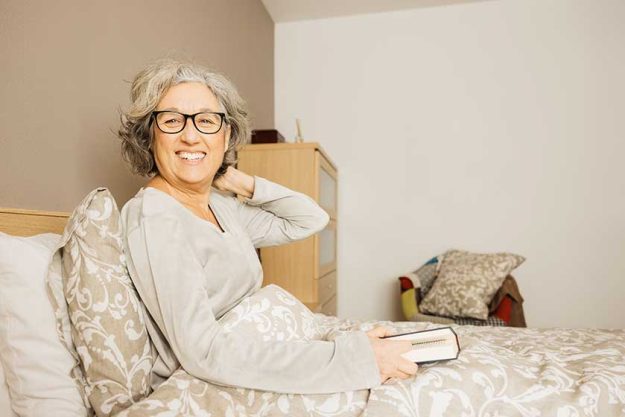 portrait senior woman sitting bed wearing pajama reading book morning