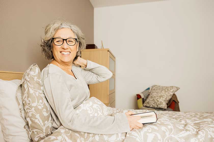 portrait senior woman sitting bed wearing pajama reading book morning