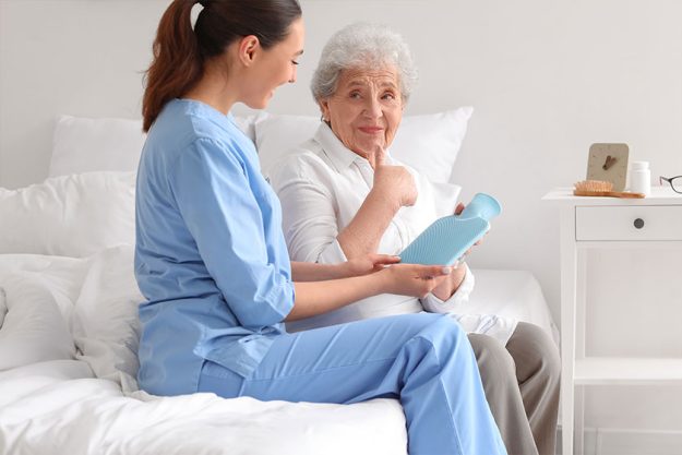 Young caregiver with hot water bottle and senior Young caregiver with hot water bottle and senior