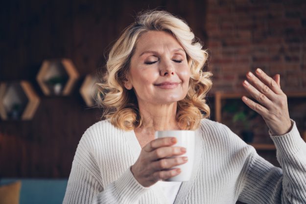 Photo portrait of lovely retired woman hold coffee smell aroma wear casual clothes cozy home interior living room in brown warm color Photo portrait of lovely retired woman hold coffee smell aroma wear casual clothes cozy home interior living room in brown warm color