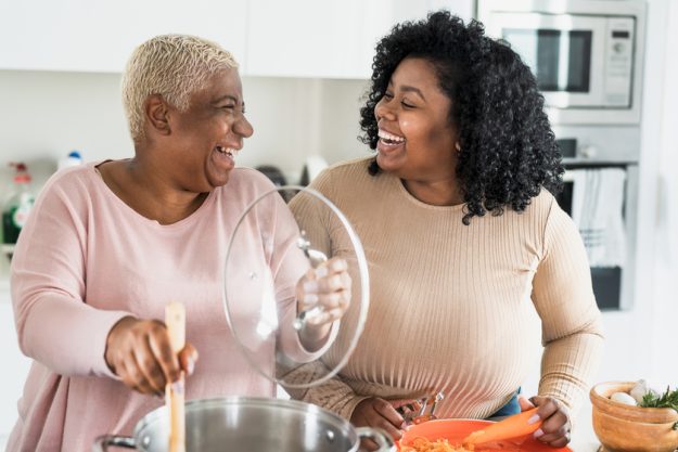 Happy Afro mother and daughter preparing lunch together in moder