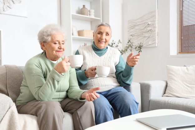 Senior female friends drinking tea on sofa at home