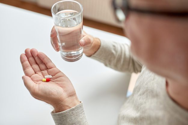 close up of old man hands with pills and water