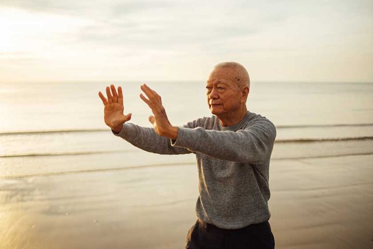 Asian senior old man practice tai chi and yoga pose on the beach Asian senior old man practice tai chi and yoga pose on the beach