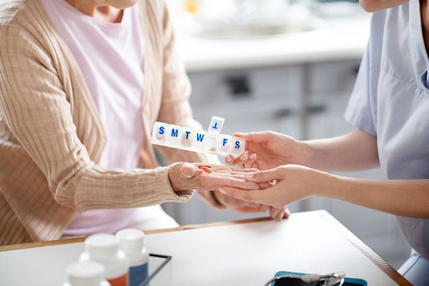 caregiver putting pills on palm of retired woman
